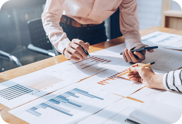 Two colleagues working together on a business plan at a table, reviewing documents and using a phone.