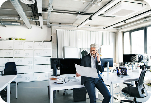 A man in a suit sits at a desk, engaged in a phone conversation.